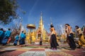 Buddhist people praying and walking around a golden pagoda.